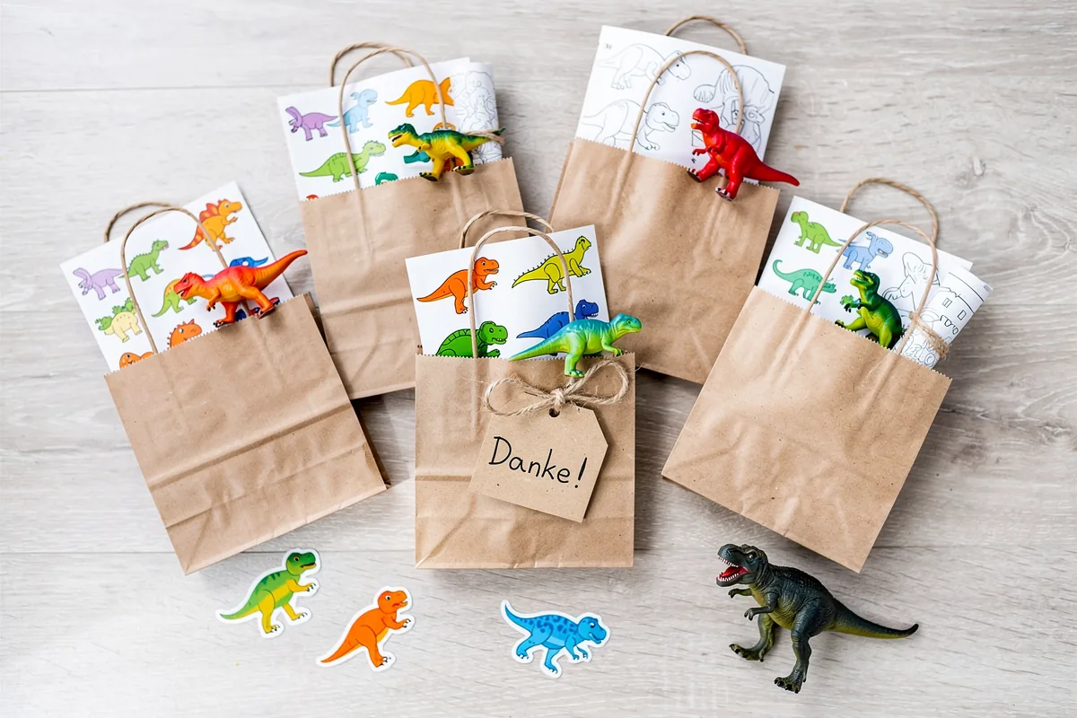 Braune Papiertüten gefüllt mit kleinen Plastik-Dinosauriern, Sticker-Bögen und Ausmalbildern auf einem Tisch