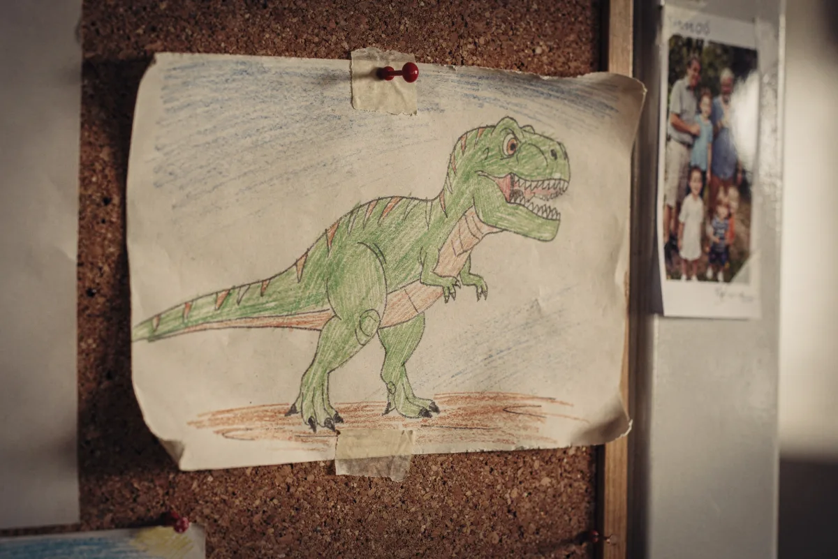 Selbst gemalter T.-rex auf einer Pinnwand mit Familienfoto — als Erinnerung an die Dino-Zeit