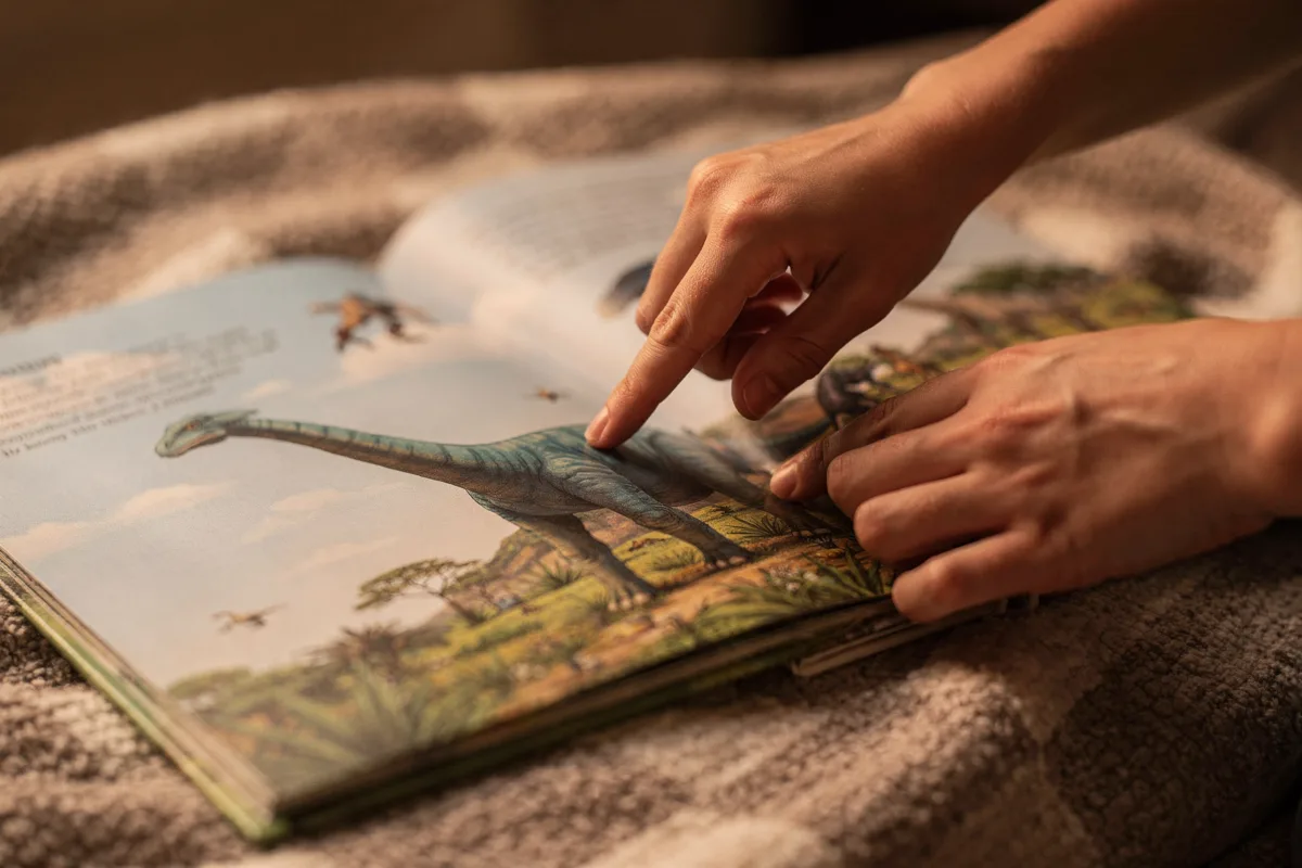 Hand zeigt im Dino-Buch auf eine Illustration eines Brachiosaurus