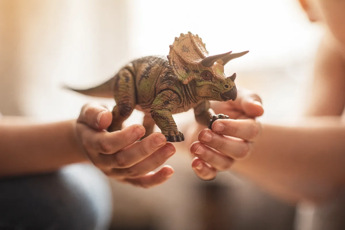 Erwachsene und kindliche Hände halten gemeinsam eine Triceratops-Figur